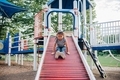 Mixed race preschooler at the park having fun sliding down a red roller slide  - PhotoDune Item for Sale