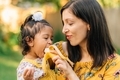 Mother and daughter in yellow, daughter taking a bite of a banana  - PhotoDune Item for Sale