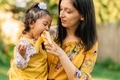 Young millennial mother and diverse daughter outside dressed in yellow eating a banana - PhotoDune Item for Sale