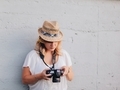 Young millennial photographer in straw hat on leaning against white wall reviewing photos on camera - PhotoDune Item for Sale