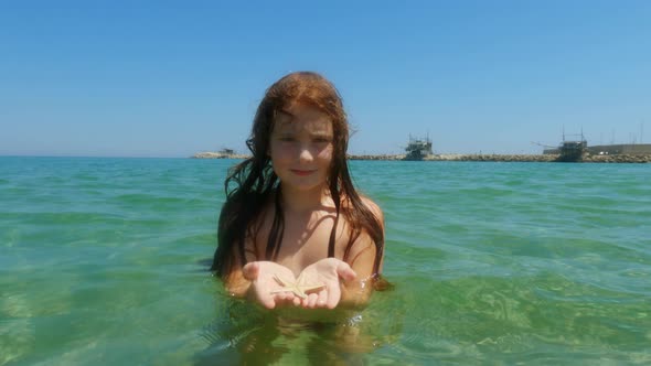 Beautiful adorable redhead child girl bathing in seawater in Italy while holding starfish in hands w