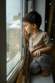 The boy sits in an apartment on the windowsill and looks at the street through the glass - PhotoDune Item for Sale