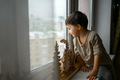 The boy sits in an apartment on the windowsill and looks at the street through the glass - PhotoDune Item for Sale