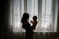 Silhouette of a mother with a baby in her arms in an apartment against the background of a window - PhotoDune Item for Sale