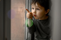A three-year-old boy sits at home on the windowsill and looks out the window - PhotoDune Item for Sale