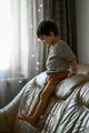 A three-year-old boy climbs over the back of the sofa. Child at home - PhotoDune Item for Sale