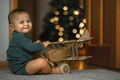 The baby at home plays with a wooden plane against the background of a Christmas tree - PhotoDune Item for Sale