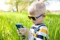 The boy sits in the backyard in the grass and watches cartoons on his phone.  People use technology - PhotoDune Item for Sale