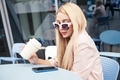 Young blond woman in casual clothes using social media on mobile phone sitting at cafe - PhotoDune Item for Sale