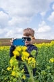 The boy takes pictures of the canola summer landscape on a smartphone. Children using technology - PhotoDune Item for Sale