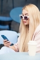 Young blond woman in casual clothes using social media on mobile phone sitting at cafe - PhotoDune Item for Sale