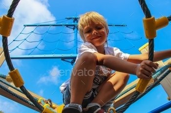 Handsome positive kid sits on the mast of a blue game ship opposite the blue sky at sunny day