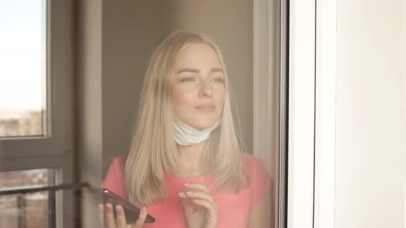 The Woman in a Protective Mask Stands at Window of Her Apartment