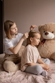 Two sisters are sitting on the bed in the room and the older sister is combing the younger one's hai - PhotoDune Item for Sale