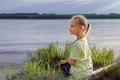 A 7-8-year-old girl sits on the riverbank and looks into the distance. - PhotoDune Item for Sale