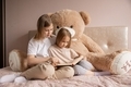Two sisters are sitting in a room on a bed with a big teddy bear and reading a fairy tale in a book. - PhotoDune Item for Sale