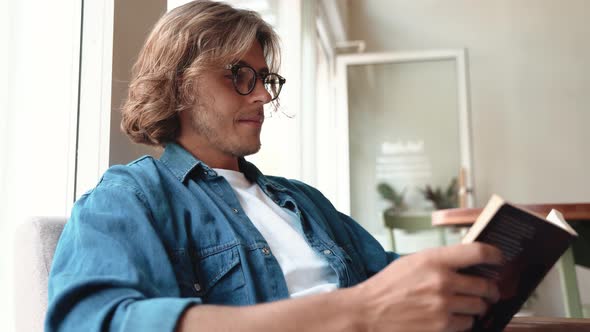 Positive blond man in eyeglasses reading book