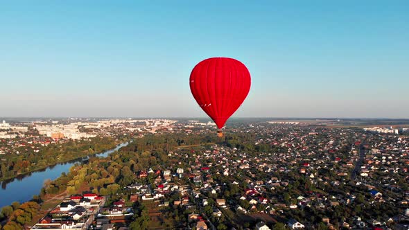 A beautiful red balloon flies in the evening over the river and the city.