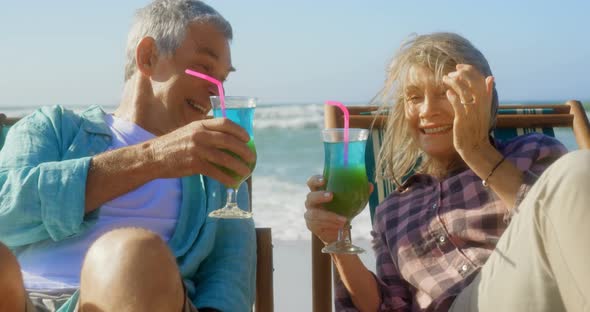 Front view of active senior Caucasian couple toasting glasses of cocktail on the beach 4k