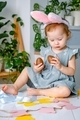 A cute smiling cheerful toddler girl dressed up bunny ears looking at easter gift chocolate eggs. - PhotoDune Item for Sale