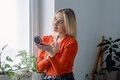 A beautiful blonde woman looking at camera making morning daily makeup using brush stands by window. - PhotoDune Item for Sale