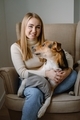 A young blonde woman sitting on armchair embracing a big mongrel domestic dog. Pets are friends. - PhotoDune Item for Sale