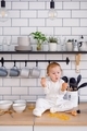 A toddler sitting on the kitchen in mess, holding broken eggs, looking surprised. Helping to cook. - PhotoDune Item for Sale