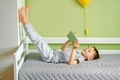 A laughing preschooler lying on the bed in a comfortable pose and using mobile phone playing a game. - PhotoDune Item for Sale