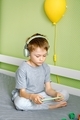A cute preschool boy in headphones watches video or plays a game engrosedly on mobile phone. - PhotoDune Item for Sale