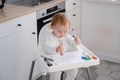 A cute smiling baby toddler sitting on a highchair and drawing first picture using colored markers. - PhotoDune Item for Sale
