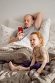 A dad with baby toddler on the bed in the morning. A young father using mobile ignoring his child. - PhotoDune Item for Sale