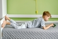 A preschooler with spine problem rachiocampsis laying on the bed using mobile. A boy with smartphone - PhotoDune Item for Sale