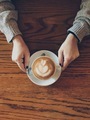 Beautiful cappuccino on a wooden table served hot and held by a woman’s hands  - PhotoDune Item for Sale