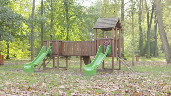 Cute Little Caucasian Girl Slides Down a Slide and Runs Away at a Playground in a Park