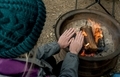 Teenage girl wearing coat and beanie warming hands over campfire at the camping site  - PhotoDune Item for Sale