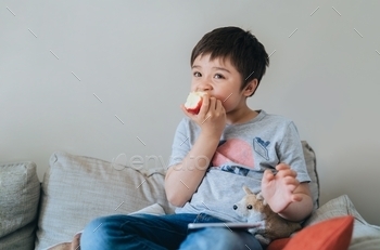 trait child eating fresh fruit. Happy boy sitting on sofa relaxing at home on weekend.