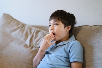 e watching TV, Happy young kid sitting on sofa relaxing in living room at home on weekend