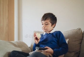  TV, Portrait child eating fresh fruit for breakfast. Happy boy sitting on sofa relaxing  befor go to school