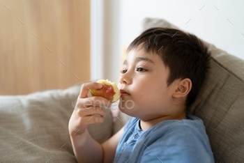 esh fruit for his snack while watching TV in living room, Close up kid face eating food. Healthy food for children concept