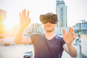 Young man with hands raised in front of him enjoying virtual reality glasses headset on city view