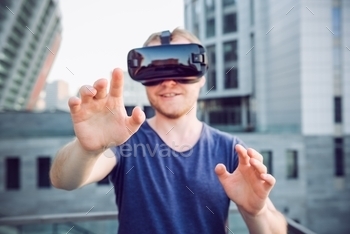 Young man enjoying virtual reality glasses headset or 3d spectacles standing against modern city