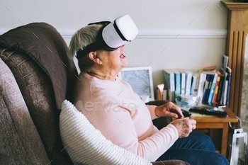 Senior woman wearing virtual reality goggles at home. Emotional lady with virtual headset