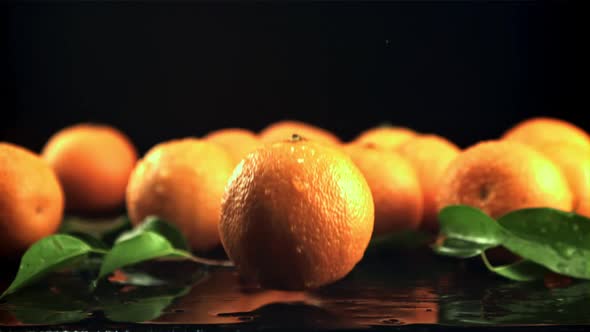 A Juicy Tangerine Falls on the Table with Splashes of Water