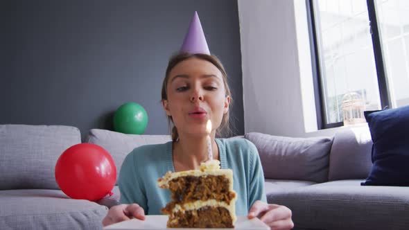 Woman in party hat blowing candle on the cake at home