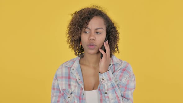 Young African Woman Talking on Phone on Yellow Background