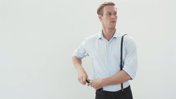 Handsome Man in Light Shirt Puts on Suspenders and Dances on White Background