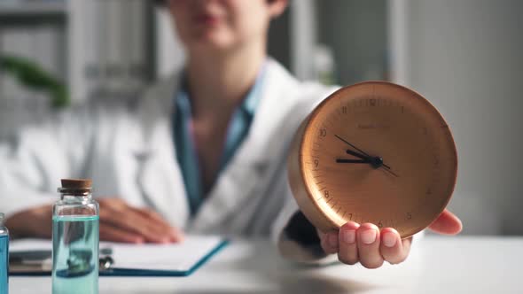 A Girl Doctor In A White Coat Sits In The Office Holding A Watch On Her Hand. Symbol Of Time Working