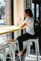 Professional businesswoman in a white t-shirt drinking coffee on a stool looking out the window - PhotoDune Item for Sale