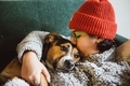 Young woman in an orange beanie and comfy sweater snuggling a comfy dog on the couch - PhotoDune Item for Sale