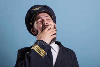pilot covering open mouth with hand. Sleepy aviation academy aircraft captain in aviation uniform with closed eyes front close view